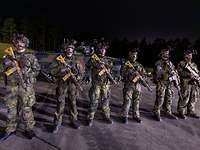 Mehrere Soldaten mit Gewehren stehen nebeneinander. Im Hintergrund ist ein Panzer zu sehen.