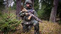 Ein Soldat mit Gewehr kniet im Wald.