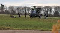 Bewaffnete Soldaten verlassen einen Hubschrauber, der auf einem Feld steht.