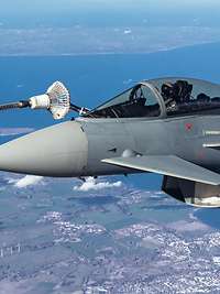 Ein Kampfflugzeug ist in der Luft an den Betankungsschlauch eines Transportflugzeuges gedockt.