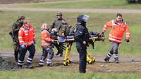 Ein Soldat liegt verletzt auf einer Trage und wird von Sanitätern abtransportiert.