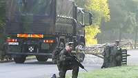 Soldaten knien auf einer Wiese und sichern einen Lkw, der durch eine Sperre aus Stacheldraht fährt.
