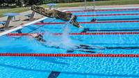 Zwei mit Uniform bekleidete Soldaten springen kopfüber in ein Schwimmbecken.