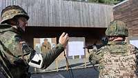 Ein Soldat steht mit Sturmgewehr im Anschlag auf einer Schießbahn, der Ausbilder daneben.