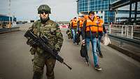 An armed serviceman escorts people wearing life jackets in the port.