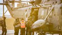 Military personnel lift a casualty on a stretcher onto a helicopter.