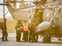 Military personnel lift a casualty on a stretcher onto a helicopter.