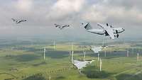 Fünf militärische Flugzeuge fliegen über einer Landschaft mit Windrädern.