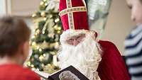 Ein Mann, verkleidet als Nikolaus, sitzt vor mehreren Kindern und liest eine Geschichte vor.
