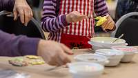 Ein Kind bestreicht ein Plätzchen. Mehrere Schüsseln stehen auf dem Tisch.