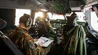Generalleutnant Freuding sitzt hinter zwei Soldaten im Cockpit eines A440M und liest ein Dokument.