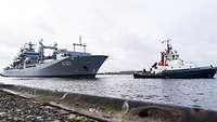 Ein großes Schiff der Marine wird von eimem Schlepper in den Hafen gezogen.