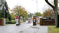 Zweispurige Einfahrt aufs Kasernengelände mit Schildern, Fahnen, Schlagbäumen und Wachhäuschen