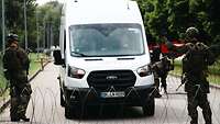 Zwei Soldaten kontrollieren einen weißen Transporter, davor und dahinter ist Stacheldraht.