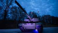Ein Panzer vom Typ Leopard 2 A8 steht auf einem Platz bei Dunkelheit und wird blau angeleuchtet.