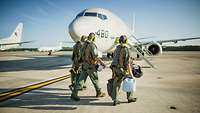 Drei Soldaten gehen auf dem Flugfeld zu einem parkenden Flugzeug vom Typ P-8A Poseidon.