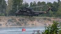 Ein Hubschrauber vom Typ CH-53 nimmt mit dem Löschwasserbehälter Wasser auf.