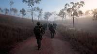 Soldaten marschieren auf einem Sandweg im australischen Buschland bei Morgennebel.