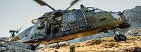 Ein Hubschrauber vom Typ NH-90 fliegt im Gebirge. Ein Soldat steht an der offenen Tür.