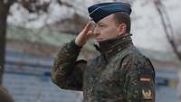 Ein Soldat grüßt mit der flachen Hand an der Kopfbedeckung.