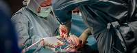 Zwei Menschen in OP-Kleidung sind über einen OP-Tisch gebeugt. Sie halten Klemmen und operieren.