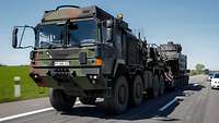 Ein Schwerlasttransporter mit einem Panzer auf dem Auflieger fährt auf einer Landstraße. 