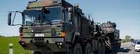 Ein Schwerlasttransporter mit einem Panzer auf dem Auflieger fährt auf einer Landstraße. 