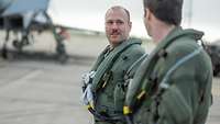 Zwei Soldaten gehen nebeneinander. Im Hintergrund steht ein Kampfflugzeug.