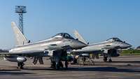 Zwei Kampfflugzeuge vom Typ Eurofighter stehen nebeneinander auf einem Flugplatz.