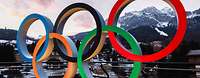 Symbolisches Foto mit einem Kunstwerk in Form der olympischen Ringe vor einer Bergkulisse