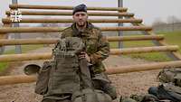 Ein Soldat mit einem Rucksack in der Hand kniet am Boden vor einem Sprungerüst.