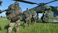 Mehrere Soldaten steigen in einen Militärhubschrauber ein, der auf einer grünen Wiese steht.