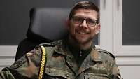 Ein Soldat mit Brille und goldener Kordel an der Schulter schaut freundlich in die Kamera