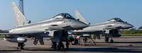 Two Eurofighter combat aircraft are parked side by side at an airfield.