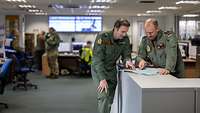 Two fighter pilots are standing at a table, looking at a map.