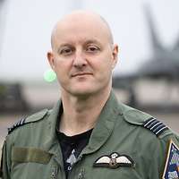 Ein Soldat im Porträt, im Hintergrund ein Kampfflugzeug