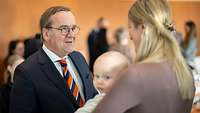 Boris Pistorius spricht mit einer Frau, die ein Kleinkind im Arm hält.