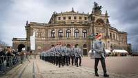 Männer und Frauen in Dienstuniform marschieren in Formation auf einen großen Platz ein.
