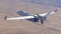Eine Drohne vom Typ MQ-9B fliegt über ein Wüstengelände.