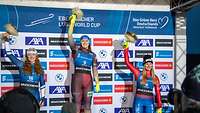 3 Frauen in Wintersportkleidung stehen auf einem Siegerpodest und halten Blumensträuße in die Luft
