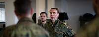 Ein General steht einem Soldaten gegenüber und spricht mit ihm, weitere Soldaten hören zu.