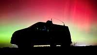 Ein Fahrzeug steht vor einem Nachthimmel mit Polarlichtern.