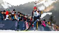 Eine Biathlon-Sportlerin fährt auf Skiern an jubelndem Publikum vorbei.