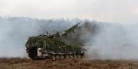 Eine Panzerhaubitze 2000 steht auf einem Feld neben einem Wald nach einem Schuss im Pulverdampf.