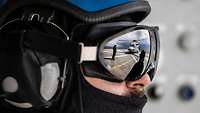 Ein Soldat mit Helm und spiegelnder Schutzbrille, auf der sich ein Helikopter spiegelt.