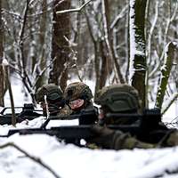 Vier Soldaten im Winter im Wald mit Waffen im Anschlag.