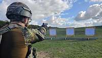 Ein Soldat mit Schutzhelm und Schutzweste schießt mit einer Handfeuerwaffe auf Holzscheiben.