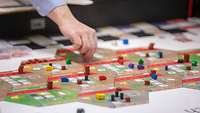 Eine Hand bewegt eine Spielfigur auf einem Brettspiel.