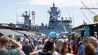Viele Besucher gehen im Hafen vor einem Schiff.