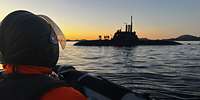 Ein Soldat sitzt in einem Schlauchboot. Im Hintergrund steht ein U‑Boot an der Wasseroberfläche.
